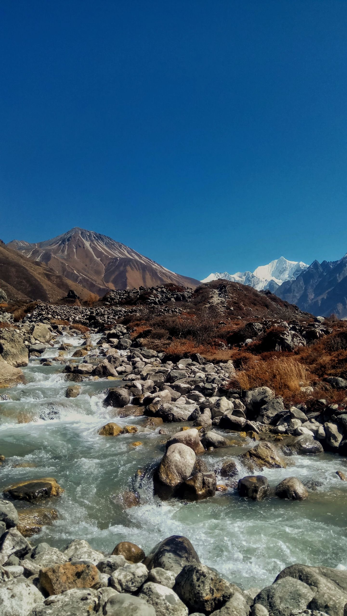 Flowing stream through rocky terrain under a clear blue sky in Langtang, Nepal.