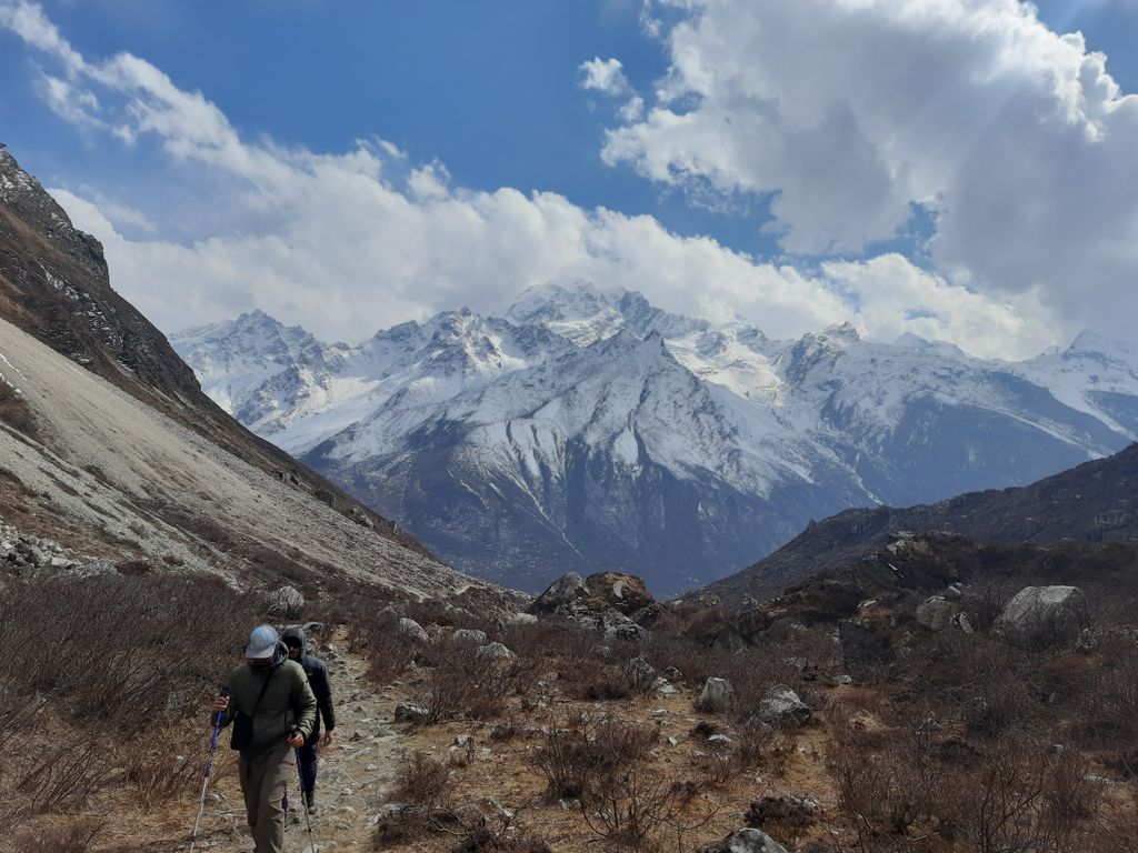 Scenic hike in Nepal's Langtang Valley with snow-capped mountains and cloudy skies.